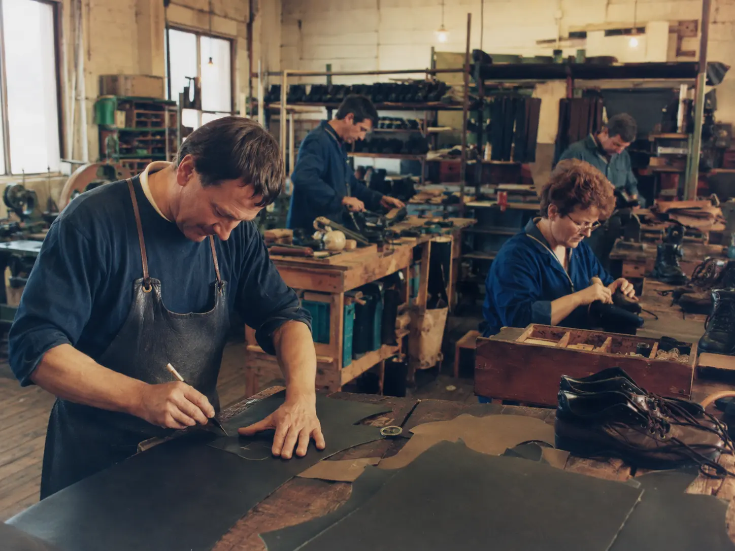 Early footwear workshop with craftspeople assembling work boots